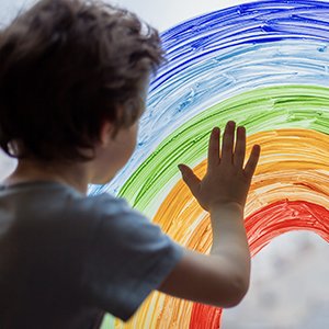 Child painting rainbow on glass